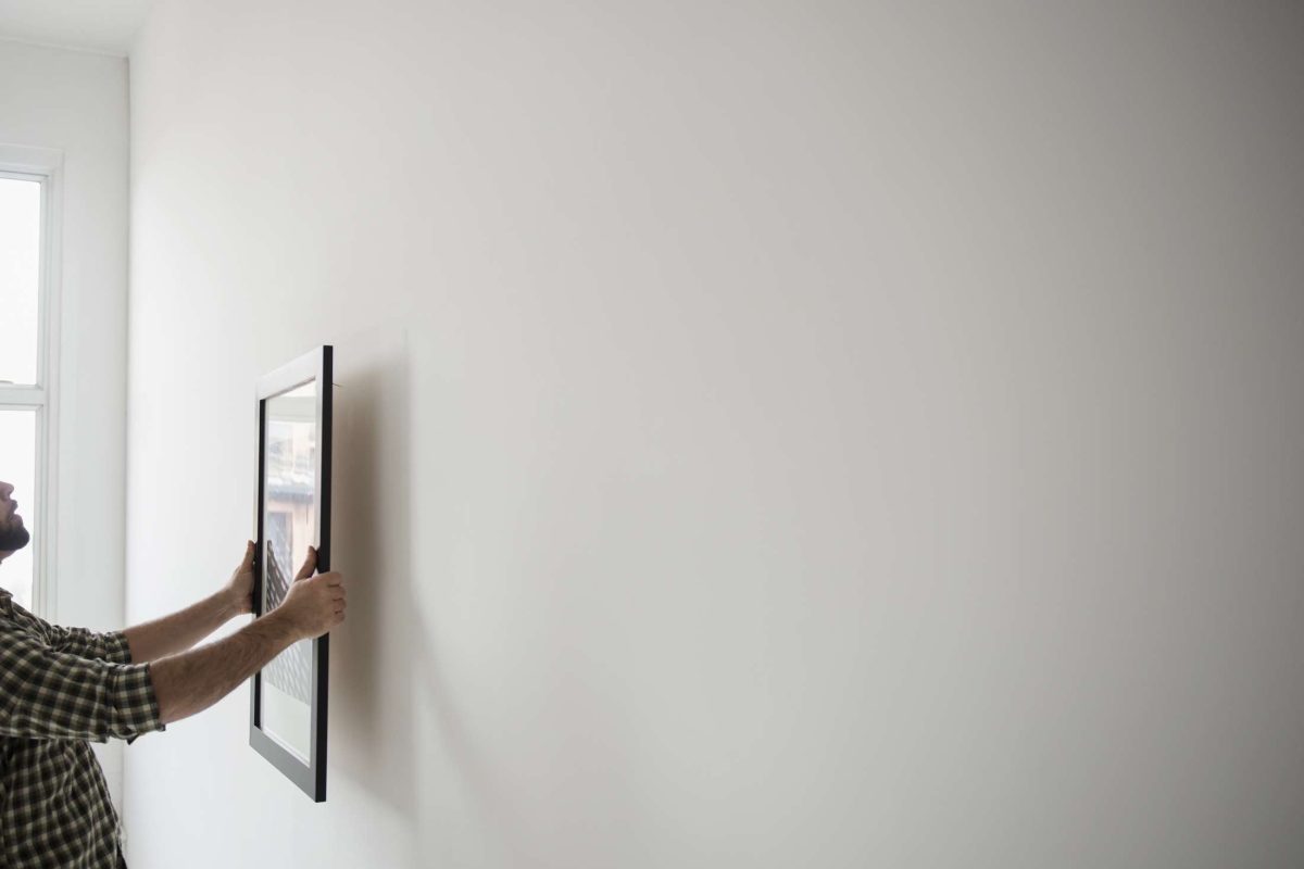 Man hanging a framed picture on a freshly painted wall โ symbolizing simple, high-ROI home improvements.