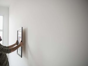 Man hanging a framed picture on a freshly painted wall — symbolizing simple, high-ROI home improvements.